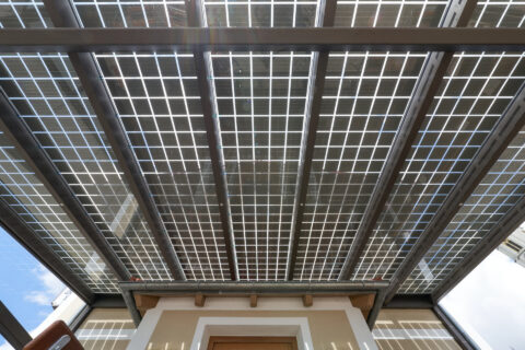 Terrassenüberdachung mit integrierten transparenten Photovoltaikmodulen zur Stromerzeugung über einem Gebäudeeingang mit Dac…