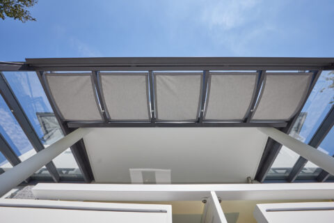 Terrassenüberdachung aus Glas mit integriertem, elektrischem Sonnenschutz und Balkonintegration in modernem Design.