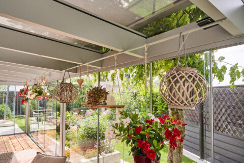 Moderne Terrassenüberdachung mit Ganzglasschiebeanlage und Beschattung, Blick in grünen Garten.