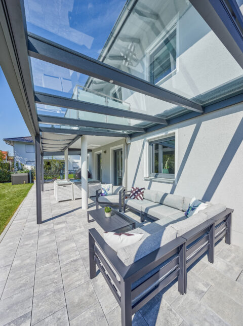 Moderne Terrassenüberdachung mit transparentem Glasdach und anthrazitfarbenen Aluminiumprofilen, ideal für entspannte Stunden.