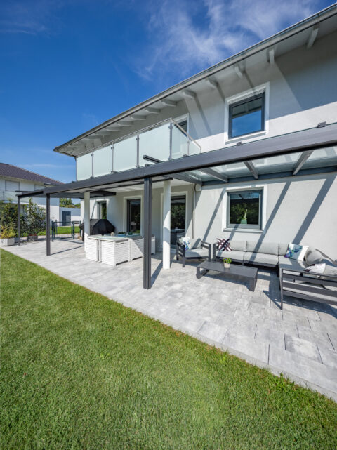 Moderne Glas-Terrassenüberdachung mit integrierten Markisen für optimalen Sonnenschutz und Komfort am Einfamilienhaus.