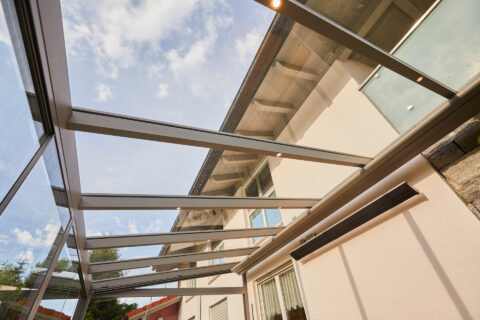 Moderne Glas-Terrassenüberdachung an einem Einfamilienhaus mit integrierter Beleuchtung.