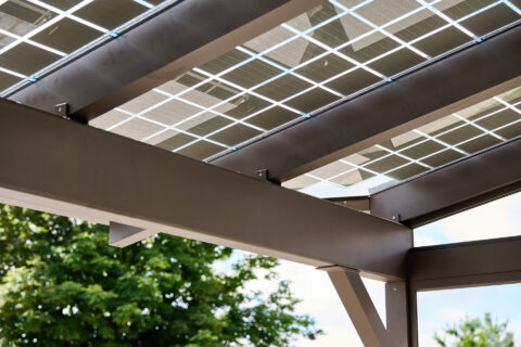 Detailaufnahme einer modernen Photovoltaik-Überdachung mit pulverbeschichteten Aluminiumträgern und transparenten Solarmodul…