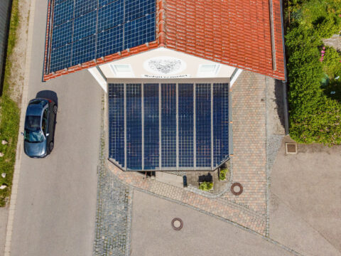 Luftaufnahme einer Gebäudeüberdachung mit integrierten Solarmodulen und weiteren Solaranlagen auf dem Dach in Niederbergkirc…