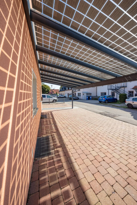 Moderner Photovoltaik-Carport mit transparenten Solarmodulen und robuster Stahl-Alu-Konstruktion vor einem Wohngebäude in Mühldorf.