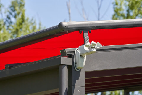Weinor Gelenkarmmarkise in kräftigem Rot auf anthrazitem Aluminium-Terrassendach mit integriertem Windwächter.