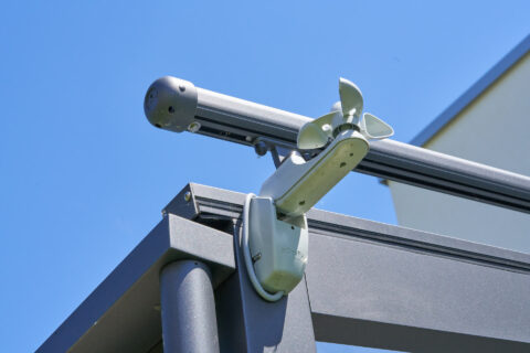 Nahaufnahme eines Weinor Windmessers, der an einer Aluminium-Terrassenüberdachung montiert ist, vor blauem Himmel.
