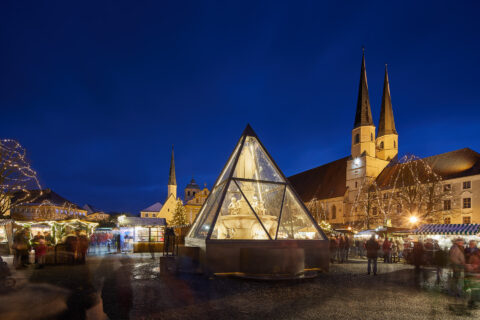 Nächtlicher Weihnachtsmarkt in Altötting mit beleuchteter Glaspyramide am Kapellplatz.