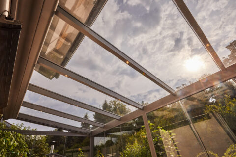 Moderne Terrassenüberdachung aus Glas und Aluminium mit integrierter Beleuchtung und ausfahrbarem Sonnenschutz.