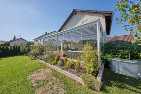 Moderne Ganzglas-Terrassenüberdachung am Einfamilienhaus in Oberpframmern, bietet Windschutz und erweiterte Wohnfläche im Ga…