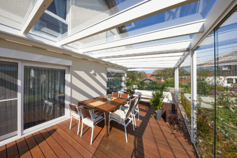 Moderner Kaltwintergarten mit Glas-Schiebewänden und integrierter Beschattung auf einer Holzterrasse in Oberpframmern