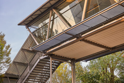 Moderner Glas-Stahl-Fußgängerüberweg mit Treppe am Bahnhof Mühldorf, verbindet Gleise barrierefrei und sicher.